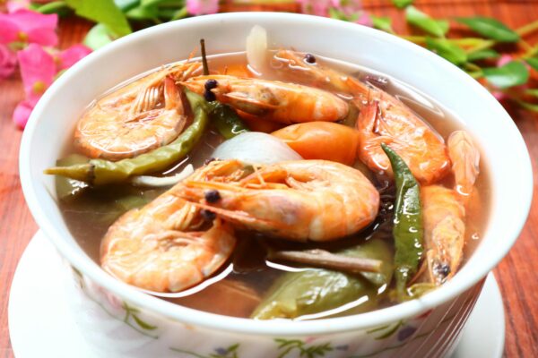 Close-up of a bowl of traditional Filipino sinigang na hipon, highlighting fresh shrimps and vegetables.